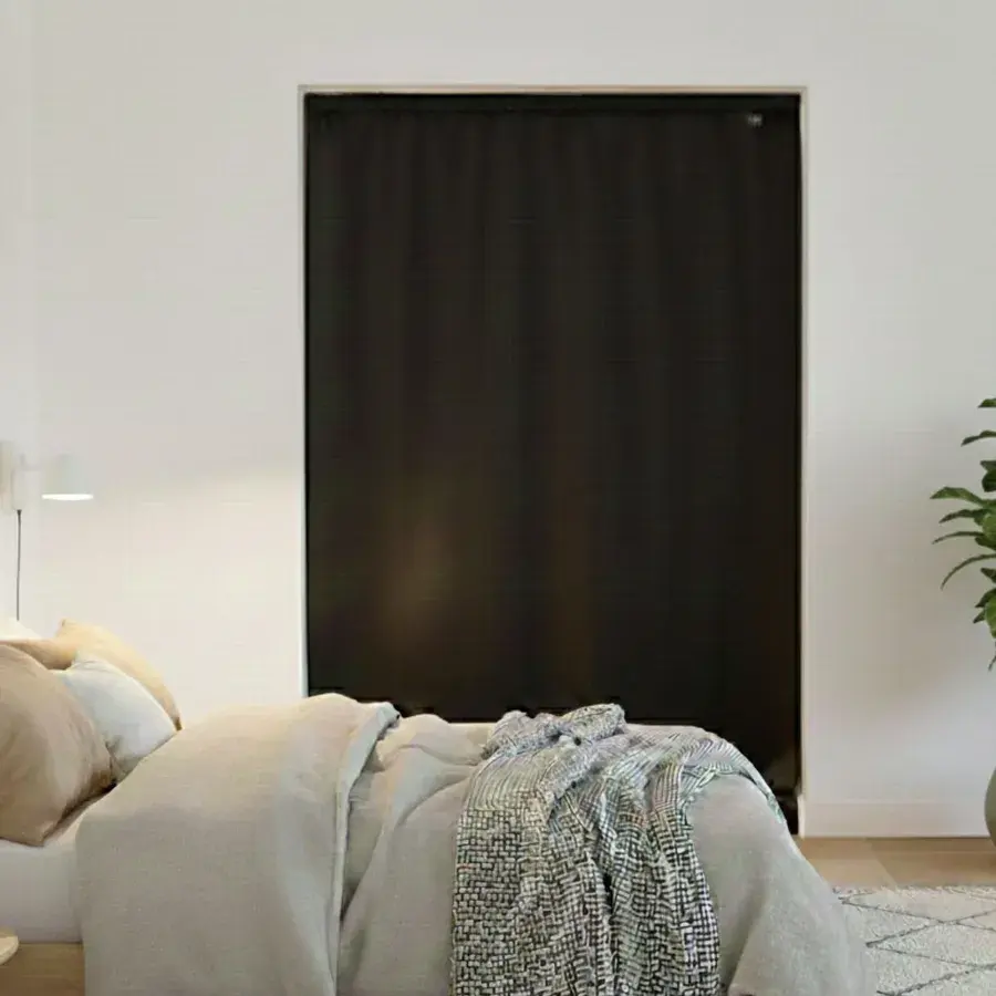 Bredt og højt sort Instant Night-gardin, der dækker en stor åbning bag en dobbeltseng
